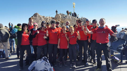 The corpuls@Alpine team poses with red team T-shirts in front of the Zugspitze summit cross
